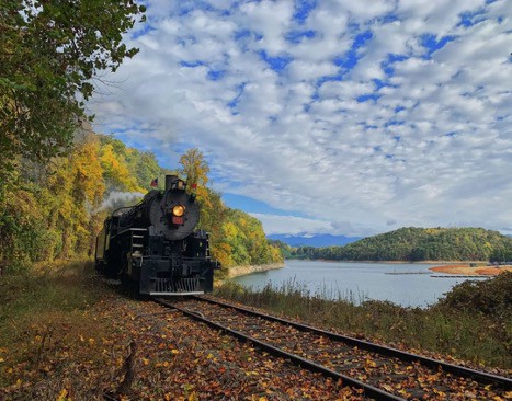 A steam train on the tracks next to a body of water.
