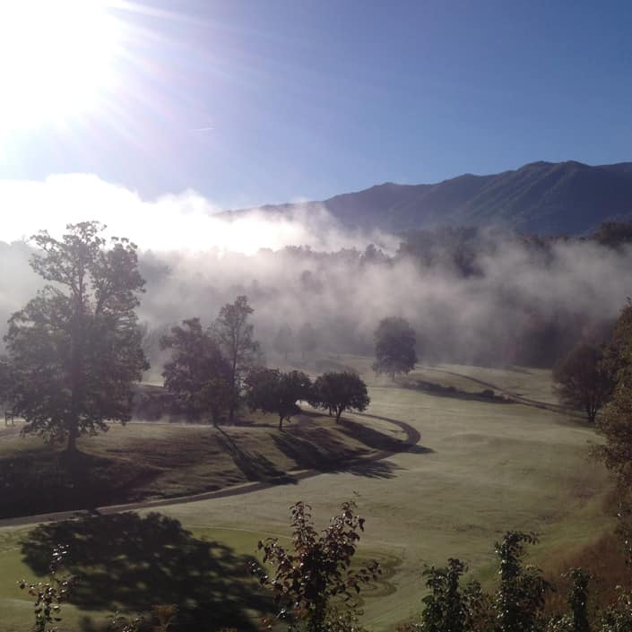 A golf course in the mist with mountains in the background.